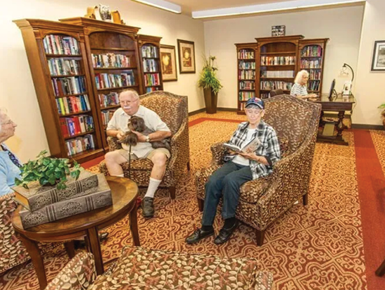 Four people are sitting in chairs in a living room, reading books. There are several books on a shelf in the background. AI generated content
