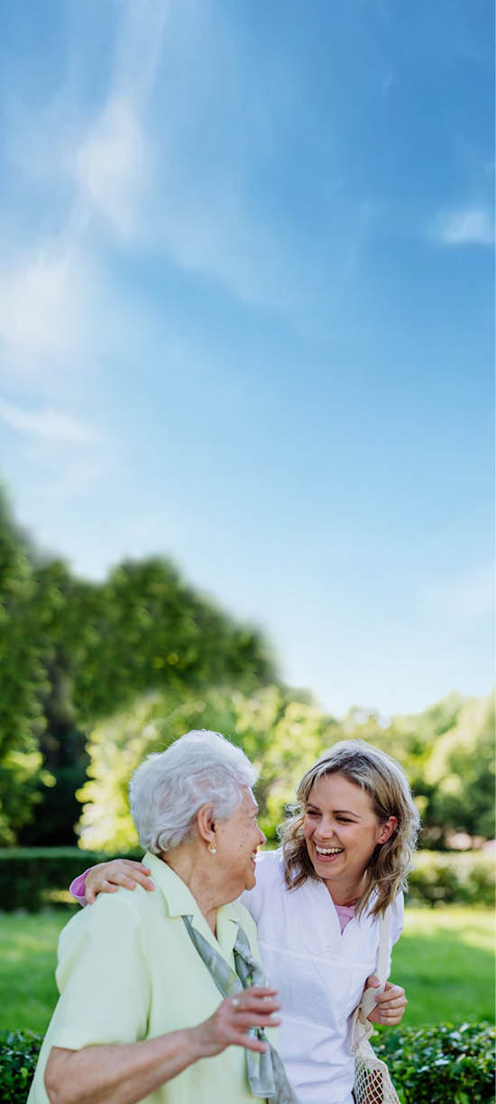 Portrait of caregiver with senior woman on walk in park.